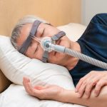 Middle aged man wearing a CPAP nasal mask while in bed.