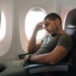 Man trying to sleep on plane and feeling uncomfortable