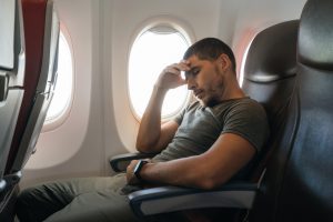 Man trying to sleep on plane and feeling uncomfortable